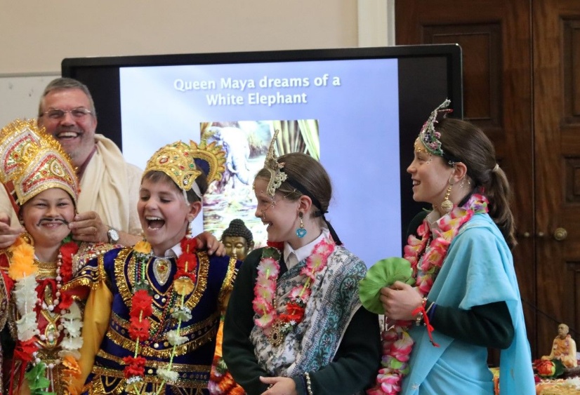 Four children dress in royal robes laugh as they take part in  a workshop with a Buddhist monk